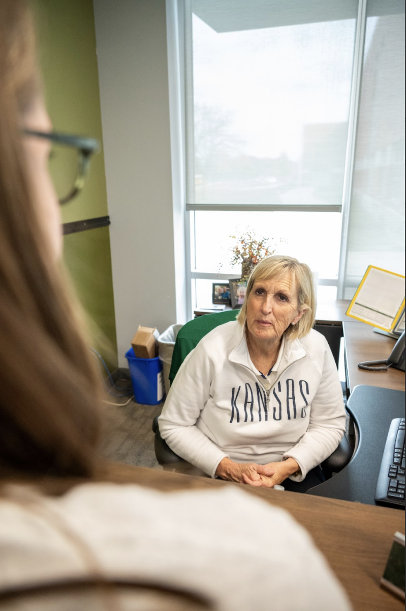 At her desk in the administrative office, Lori Queen speaks with a student. 